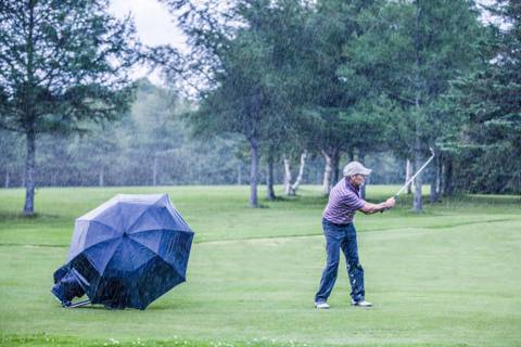 Golfer teeing off in the rain with a golf umbrella